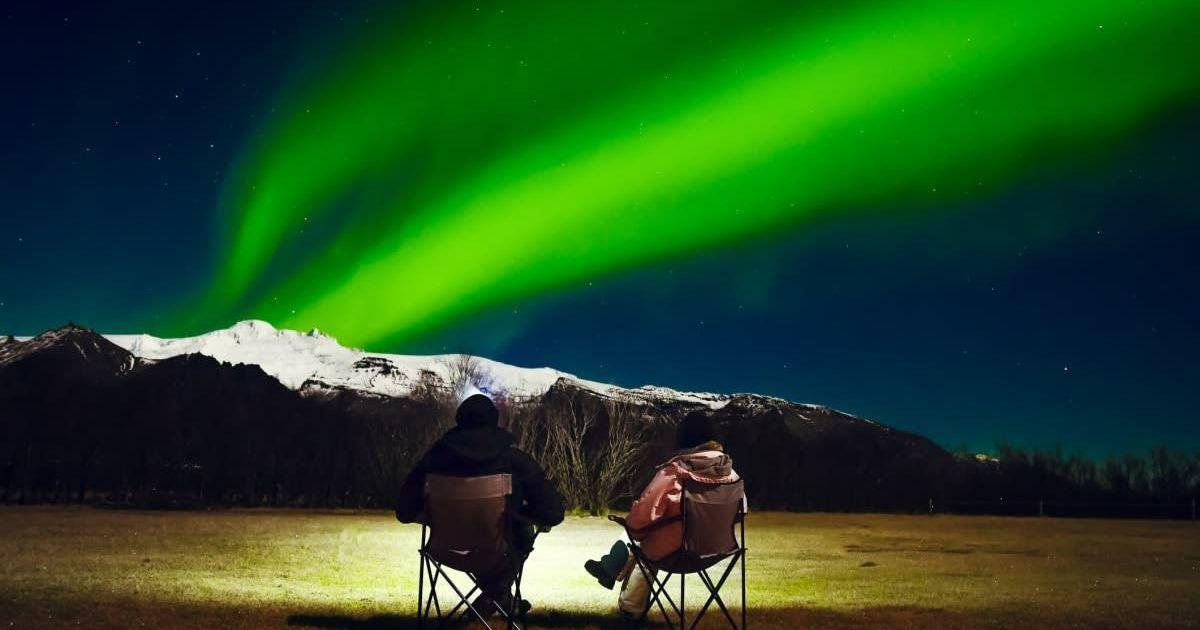 A couple sits in foldable camping chairs, watching the Northern Lights (Representative Cover Image Source: Getty Images | EvaL)