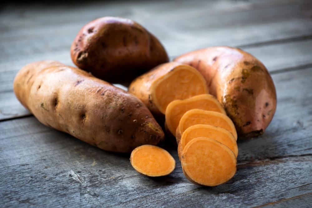 Sweet potatoes and slices on a wooden surface.