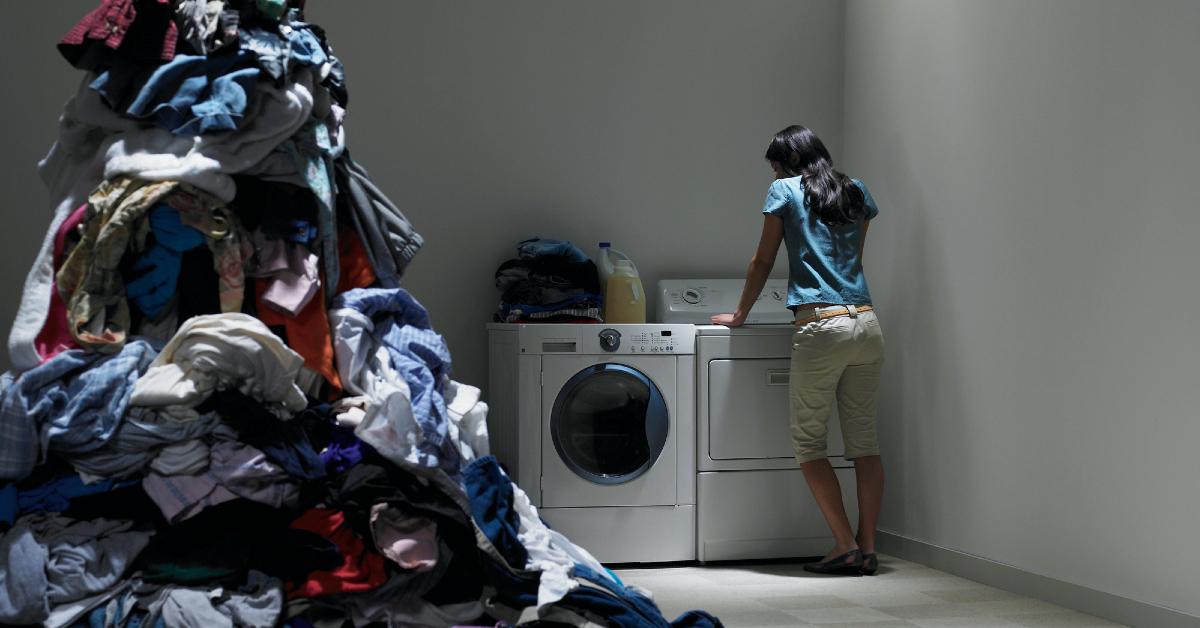 Photo of woman standing in front of a washer and dryer and beside a mountain of dirty laundry