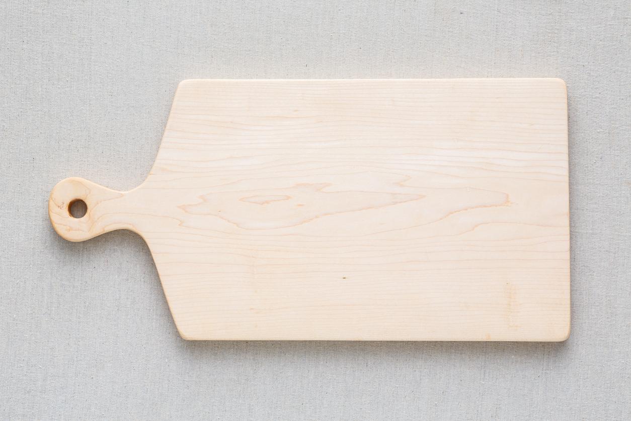 A handmade maple wood chopping board is pictured against white-gray linen. 