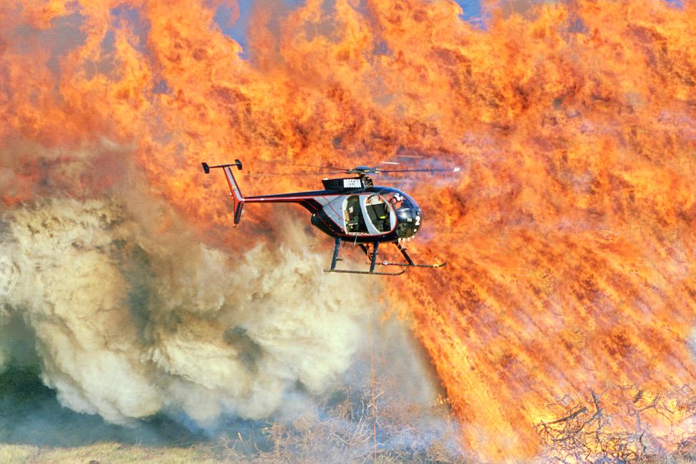 A helicopter flying by a massive fire. 