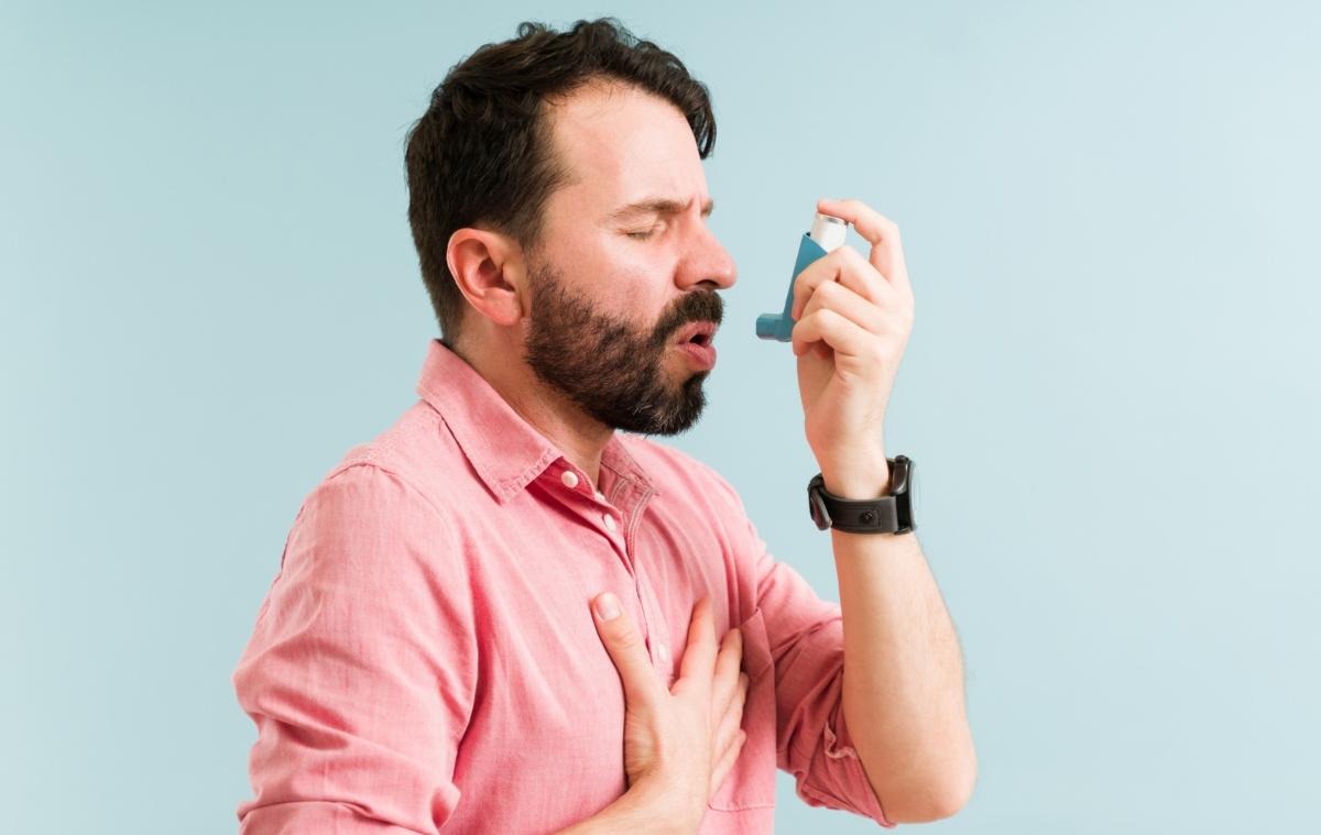 Man in pink shirt using an inhaler.