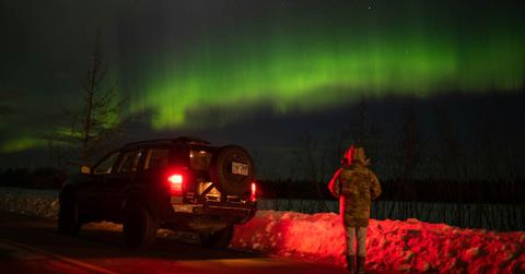 A man standing beside a car, looking at auroras in the sky. (Representative Cover Image Source: Pexels | John De Leon)