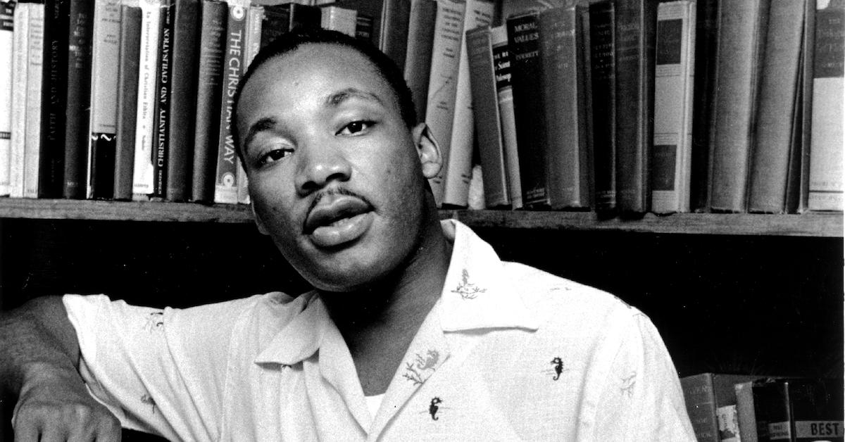 Martin Luther King Jr. poses in front of a bookcase in a black-and-white image.