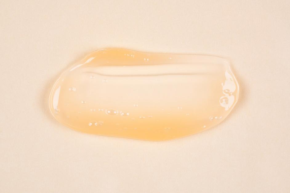 Cosmetic serum with a yellow tint in front of a light background. 