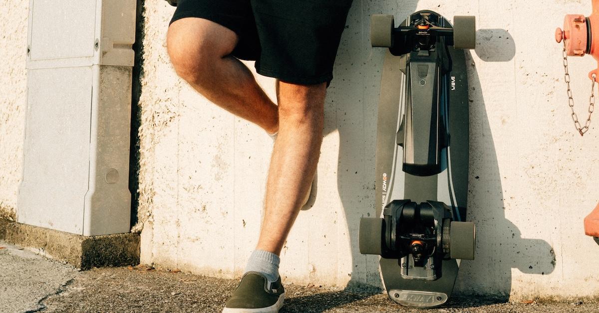 Man leans against wall alongside an electric skateboard by Exway