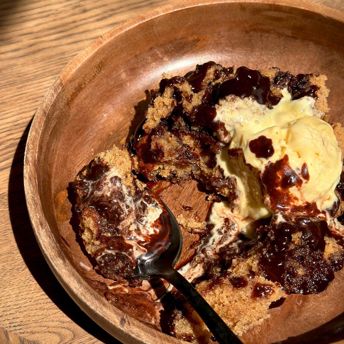 Photo of Ruby Bhogal's Plant-Based Self-Saucing Sticky Toffee Pudding Sheet Cake with Stem Ginger and Chocolate in a wooden bowl taken by Bhogal herself