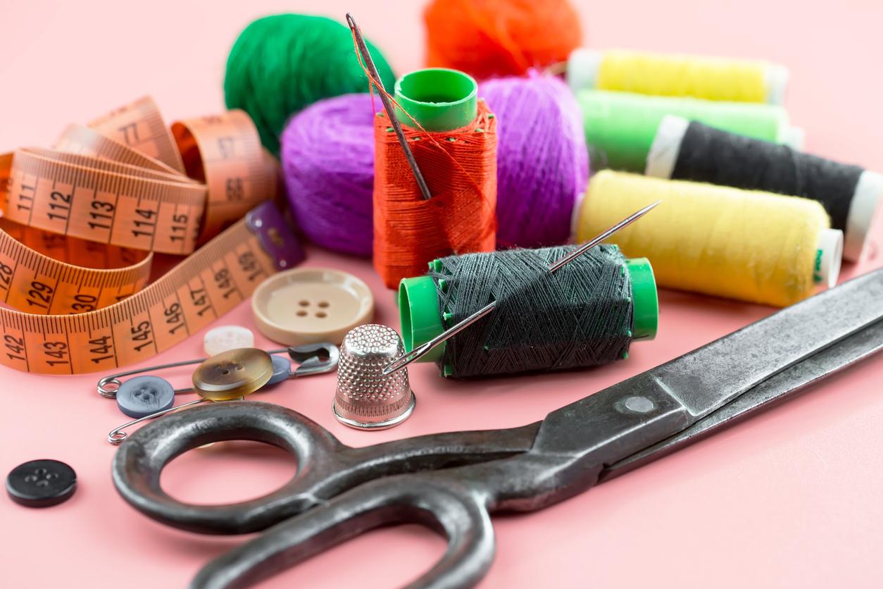 Various hand sewing supplies like thread, needles, scissors, a tape measure, and buttons on a pink table.