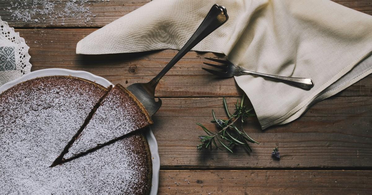 A brown cake sprinkled with white powdered sugar sits atop a table set up for a gathering