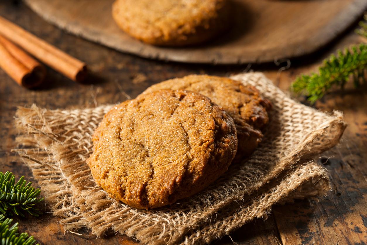 Gingersnap cookies are pictured atop a burlap napkin on a wooden table.