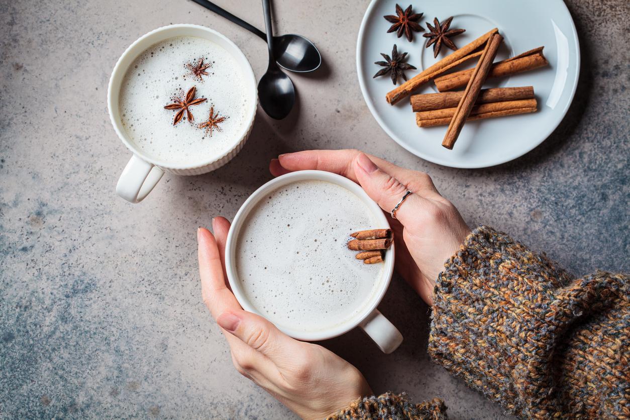 A person holds one of two cups of chai tea with cinnamon sticks inside it for added flavor.