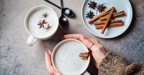 A person holds one of two cups of chai tea with cinnamon sticks inside it for added flavor.