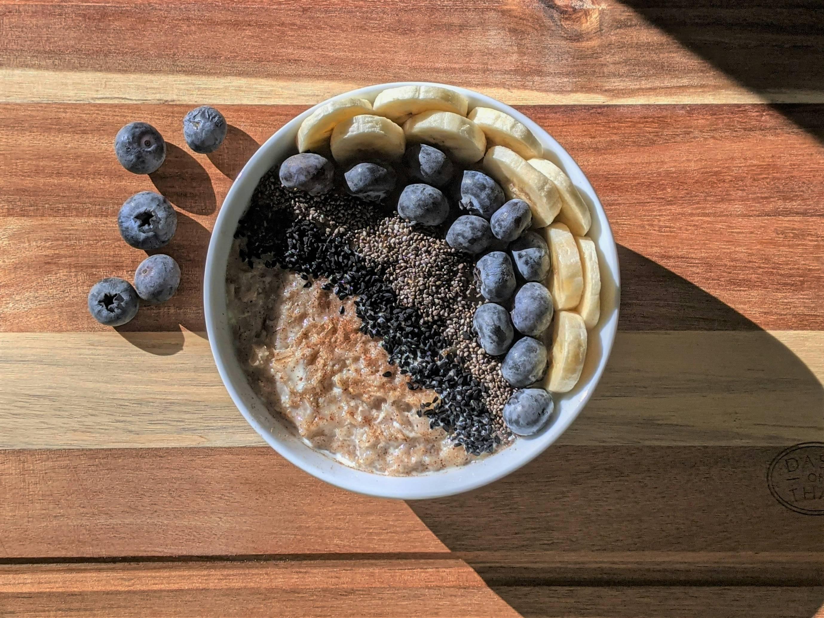 A bowl of oatmeal is supplemented by blueberries, bananas, and various seeds.