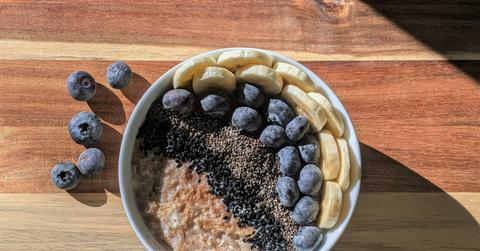 A bowl of oatmeal is supplemented by blueberries, bananas, and various seeds.