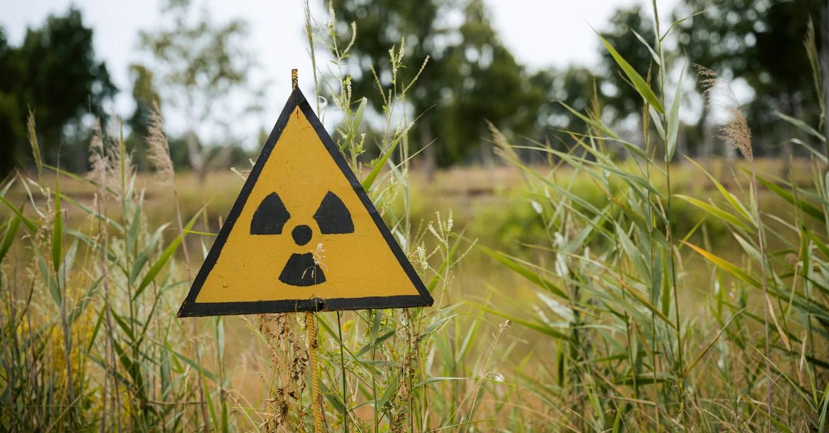 A black and yellow radioactive warning sign appears in a grassy field 