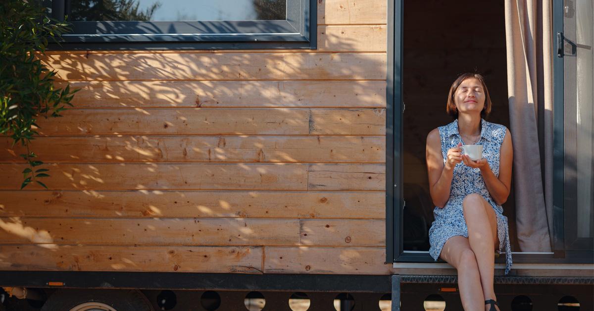 woman drinking coffee on the stairs of her tiny house 