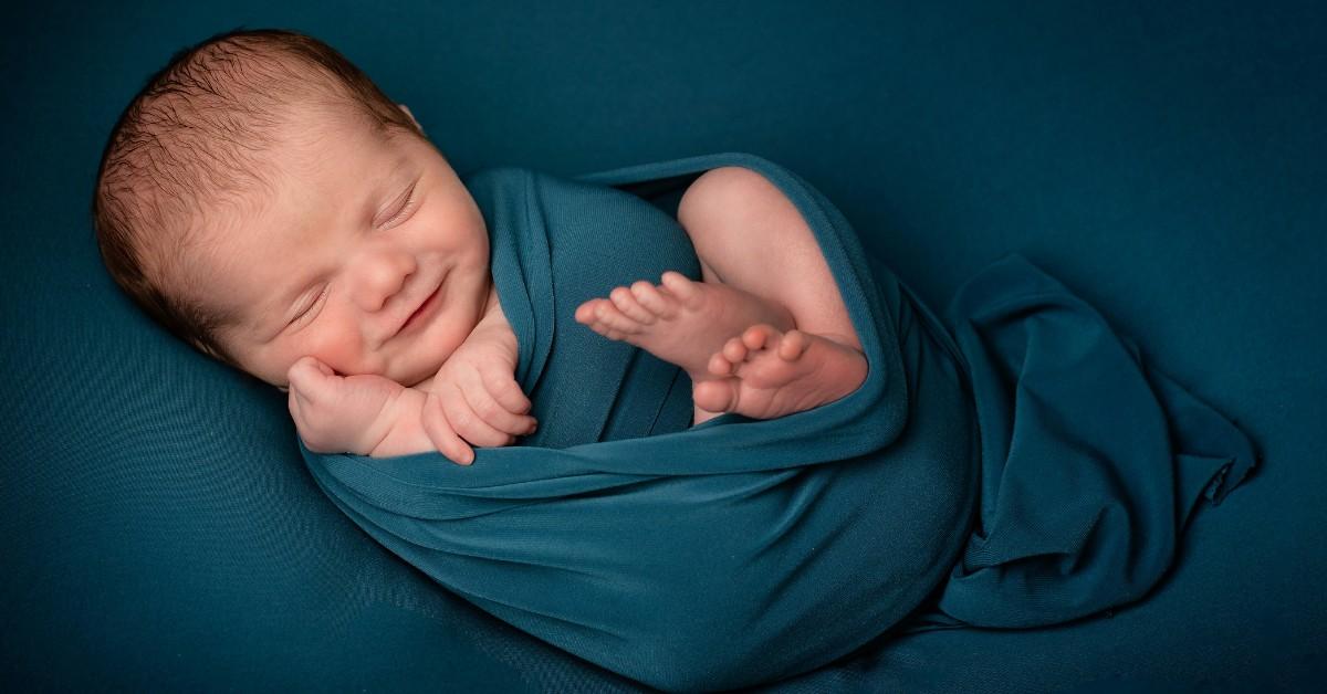A newborn baby is swaddled in a blue wrap