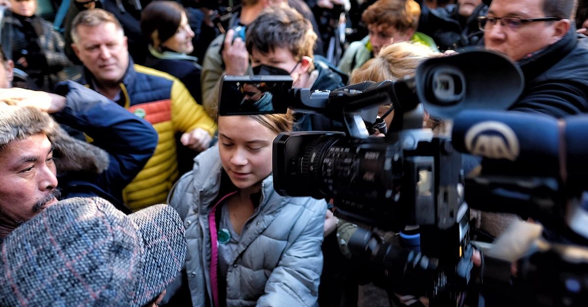 Greta Thunberg outside of court, in a crowd of people, with a video camera on her face