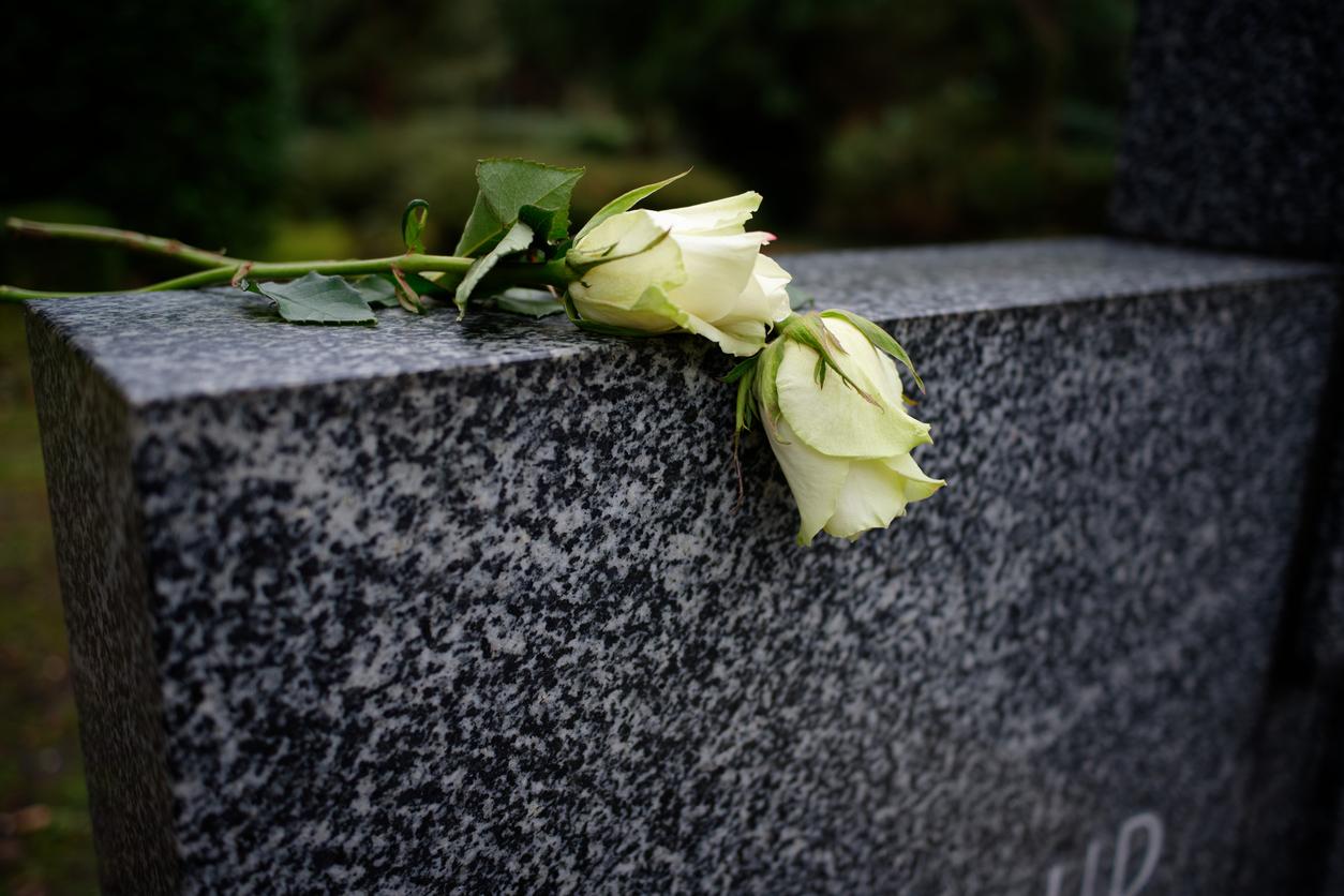 A black marble headstone with two white roses on top.