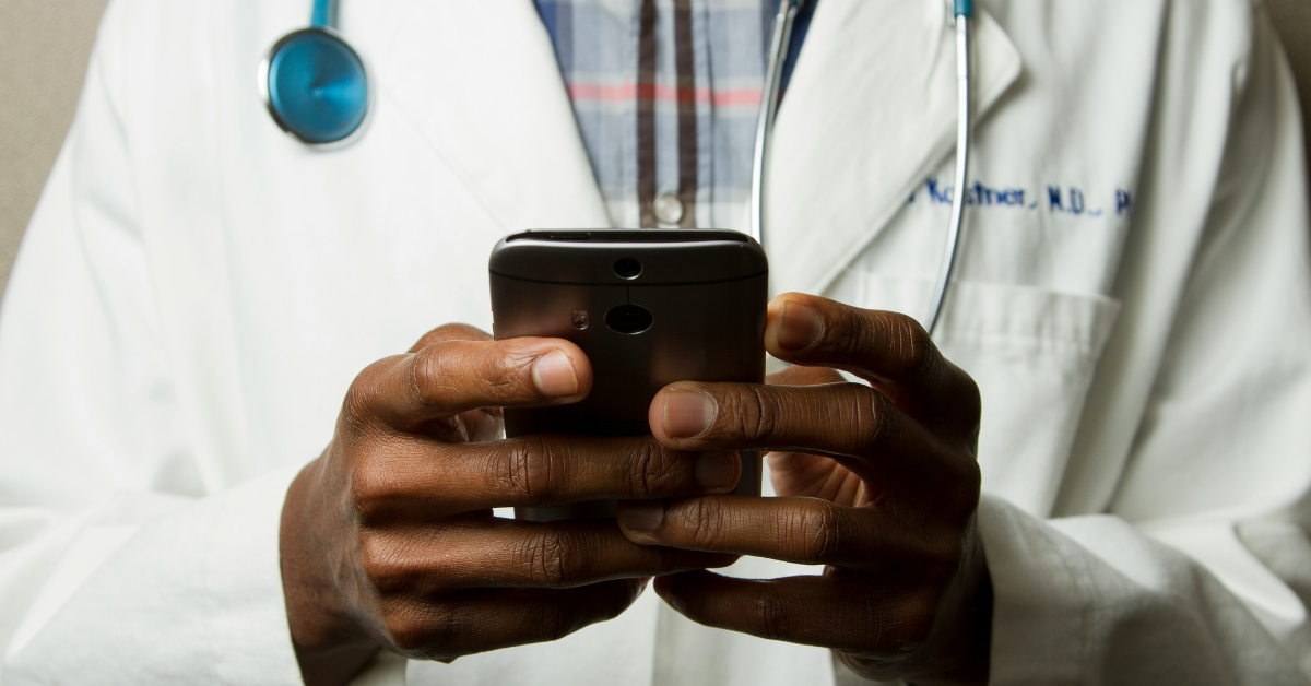 A doctor wearing a white coat holds his cell phone while wearing a stethoscope 