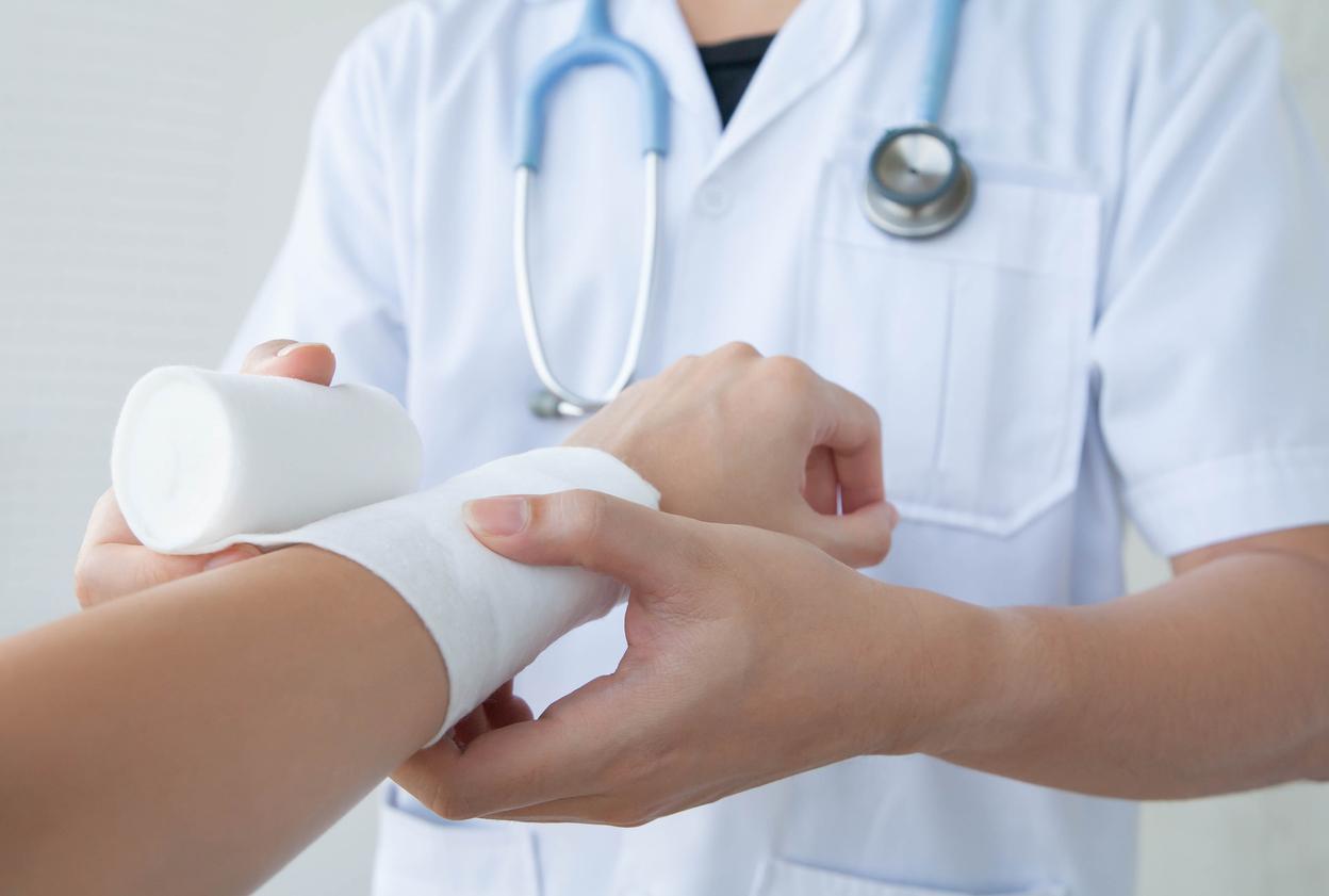 A doctor wraps a bandage around a patient's wound on his arm.