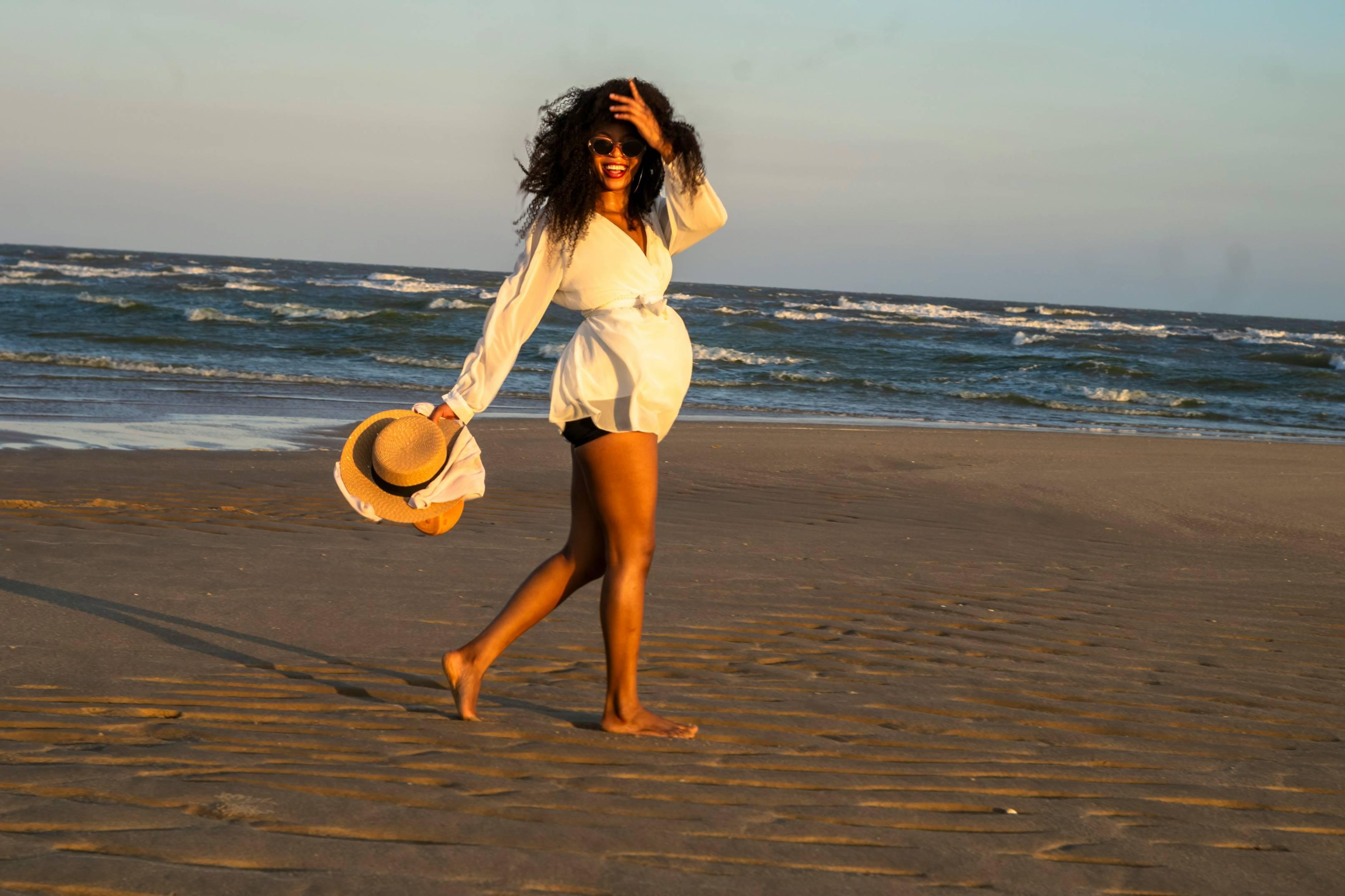 A smiling woman walks barefoot on the beach.