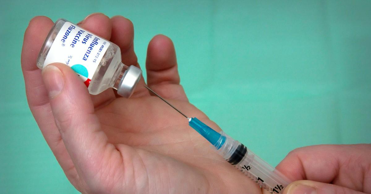 A person uses a syringe to draw out the flu vaccine