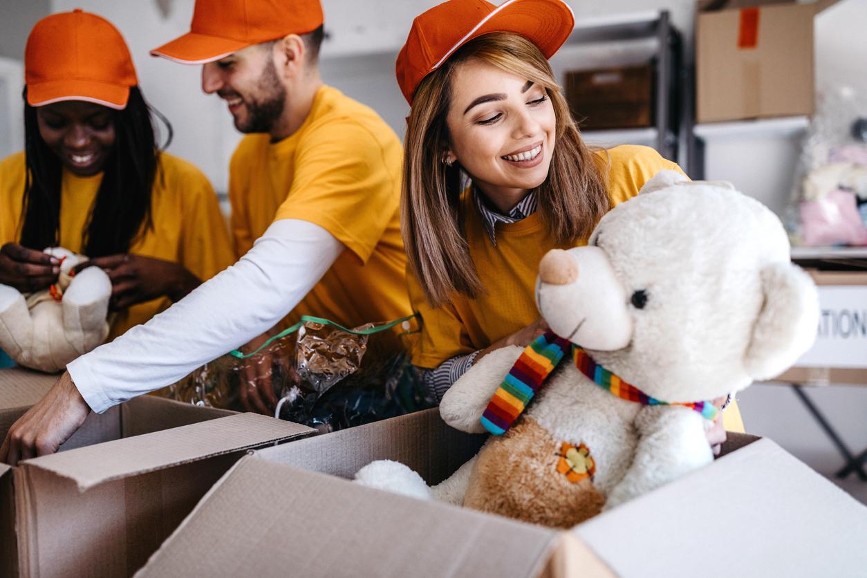 Three smiling volunteer workers inspect donations and items for recycling, including a large white bear.