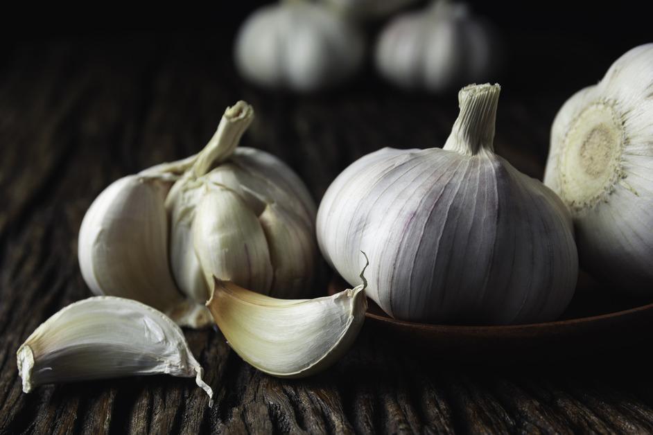 A close up photo of several garlic bulbs on a table with two cloves in front of them. 