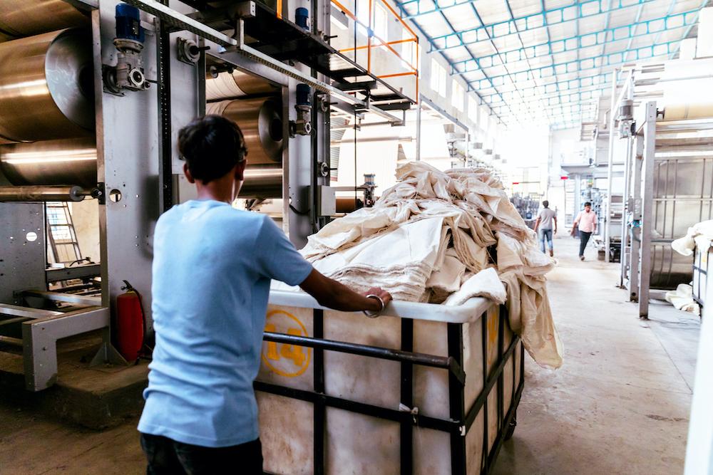 A textile worker pushes a cart of fabric in a factory.