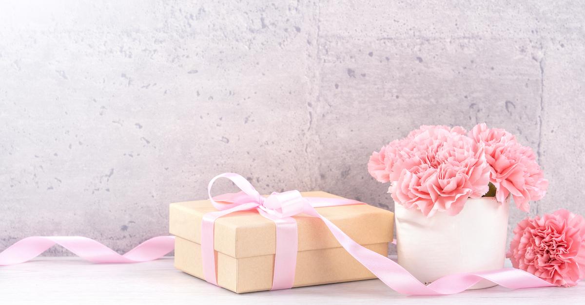 A box wrapped in pink ribbon, next to a pink bouquet.