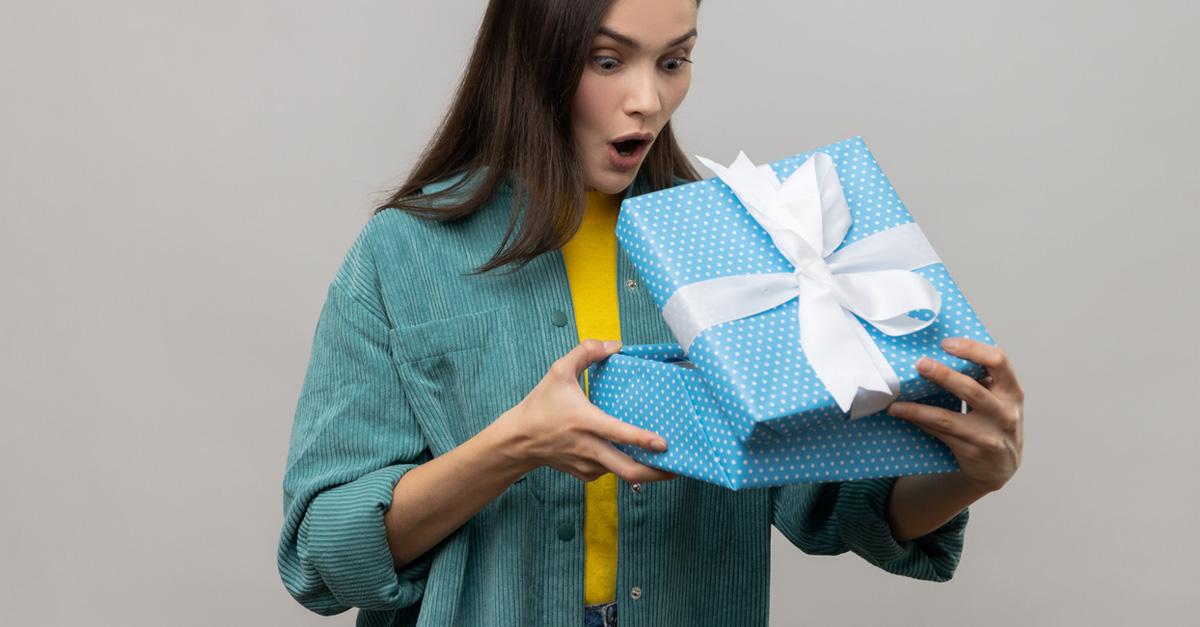 woman in green shirt looking inside a blue gift box with white bow