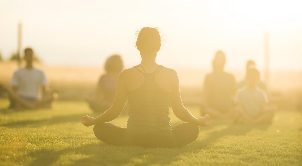 People sitting on grass in an outdoor yoga class. 