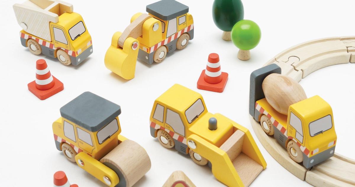 Wooden toy trucks, trees, and traffic cones sit on white surface.