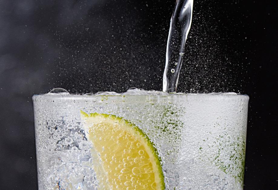 A close up of sparkling water being poured into a glass with a lime slice. 