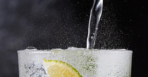 A close up of sparkling water being poured into a glass with a lime slice.