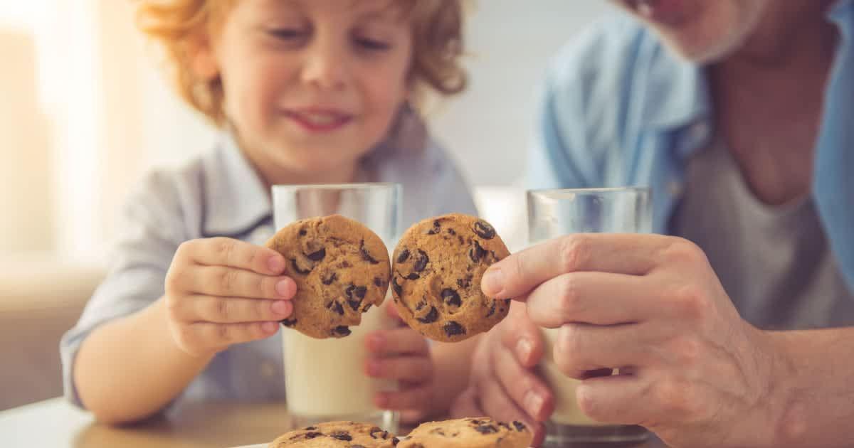 Parent and kid picking cookies from a plate while glasses of milk sit on the table. (Representative Cover Image Source: Getty Images | Vadimguzhva)