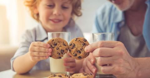 Parent and kid picking cookies from a plate while glasses of milk sit on the table. (Representative Cover Image Source: Getty Images | Vadimguzhva)