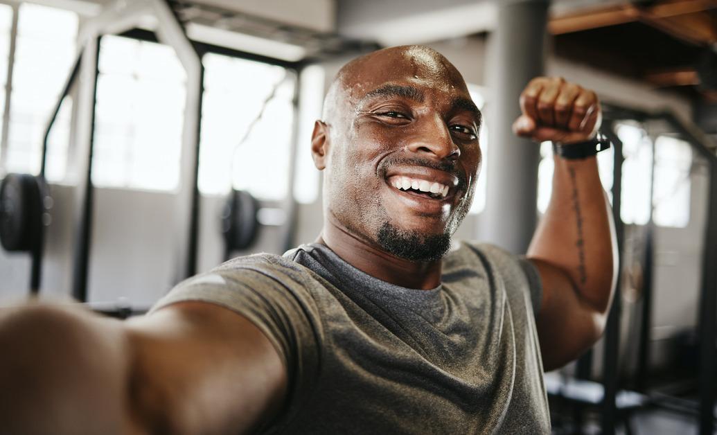 A man taking a selfie at the gym and flexing his arm muscles. 