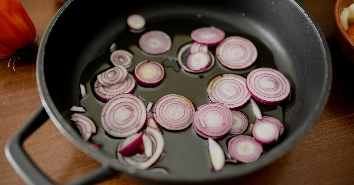 Red onions frying in vegetable oil in a cast iron pan.