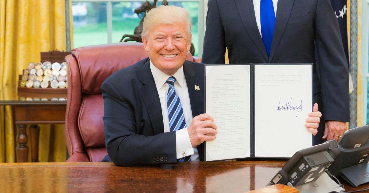 Donald Trump smiles while holding up a signed form
