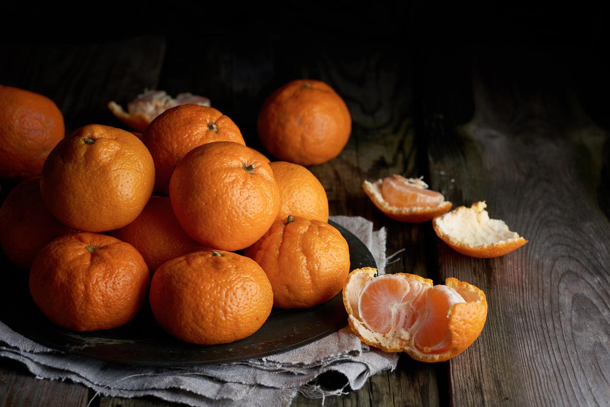 Mandarins are stacked on top of one another on a dark plate, with two mandarins opened on a wood table.