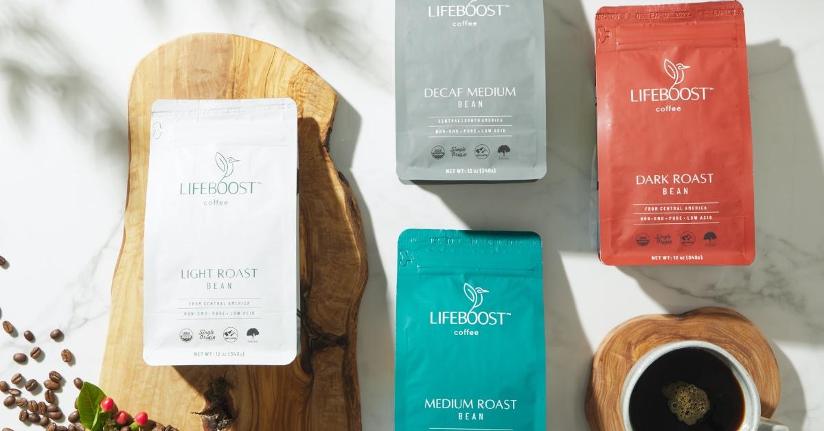 Four bags of Lifeboost Coffee alongside a mug on a tabletop