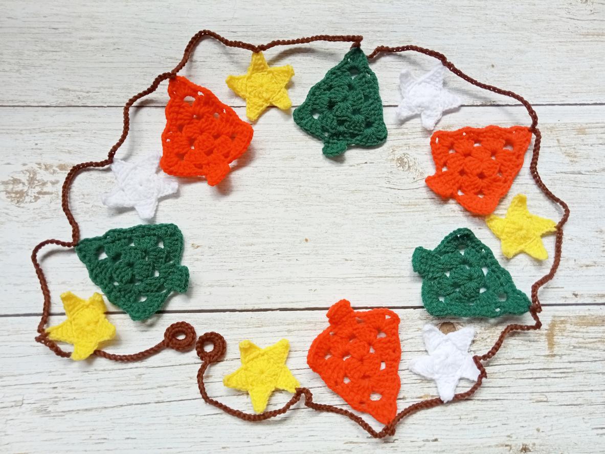 A crocheted garland comprised of red and green trees with white and yellow stars in between them.