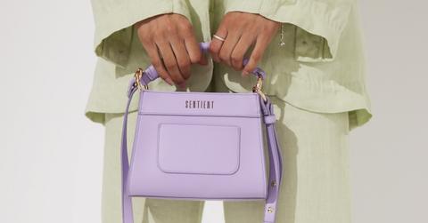 Someone in a light green suit holds a light purple Sentient purse