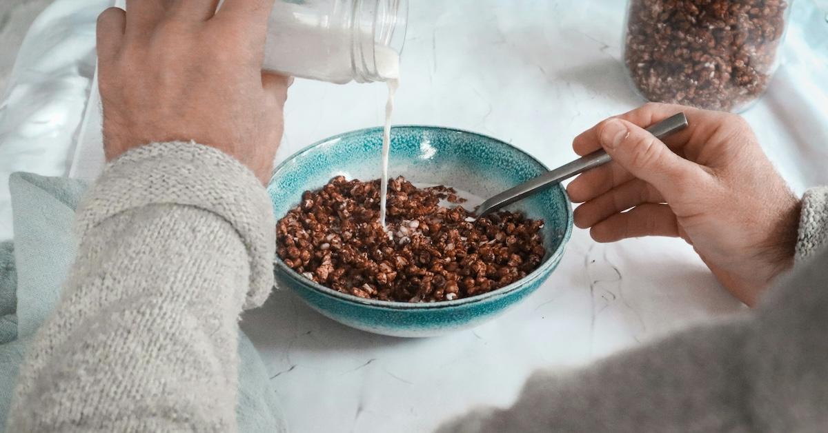 Person pours milk into blue ceramic bowl of cocoa cereal.