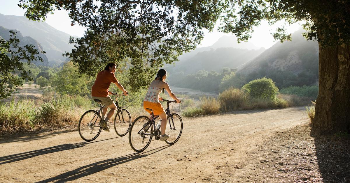 Two people riding bikes along a dirt path. 