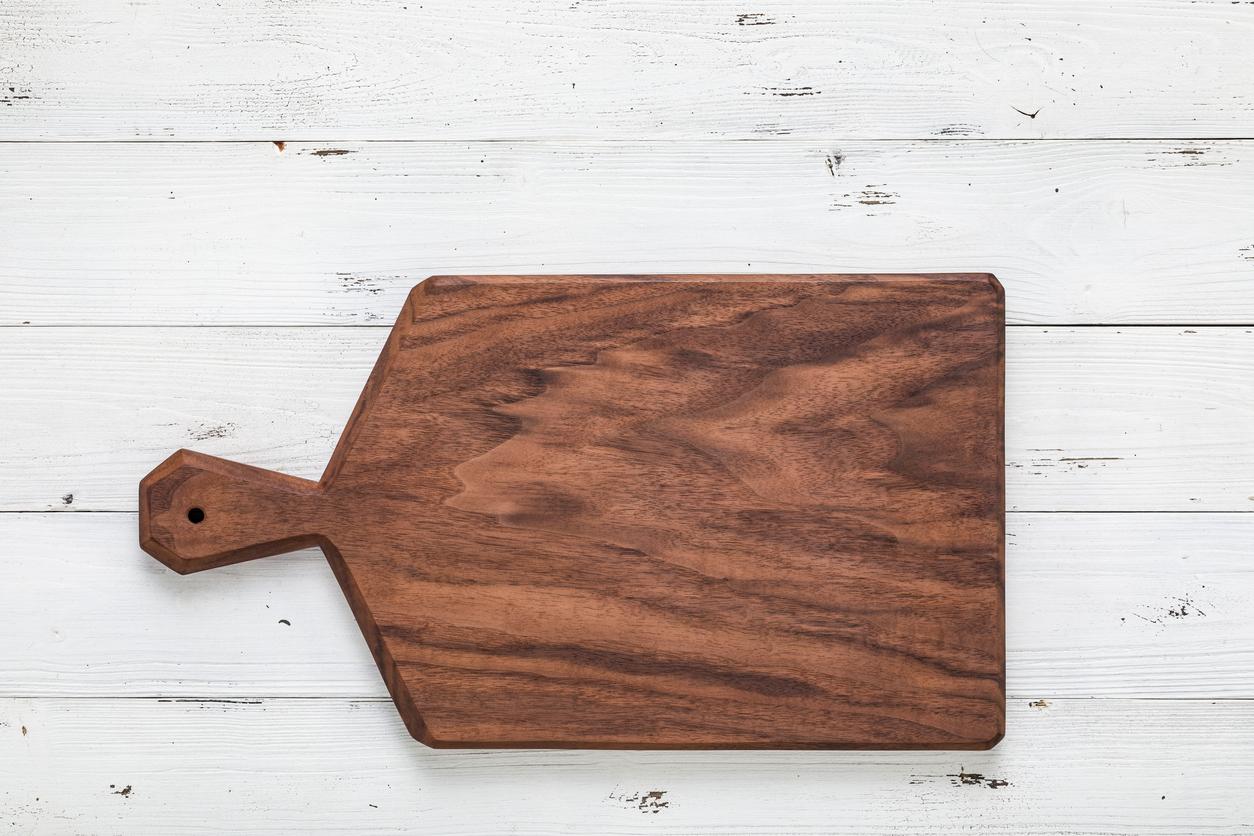 A handmade walnut chopping board is pictured against white wood panels. 