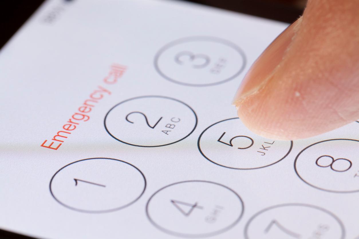 A close-up photo of a person's finger tapping numbers on a smartphone with "Emergency call" labeled at the top.