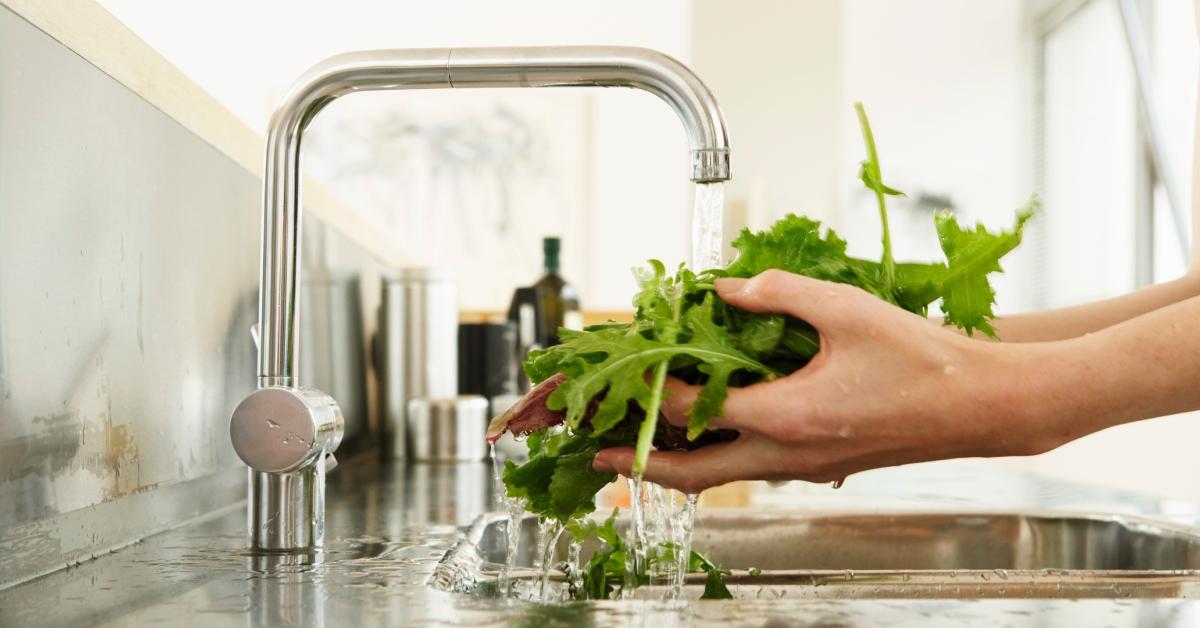 A person washes a handful of lettuce under the sink.